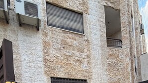 Un edificio de piedra con una escalera que lleva a un balcón, unidades de aire acondicionado y una barandilla metálica.