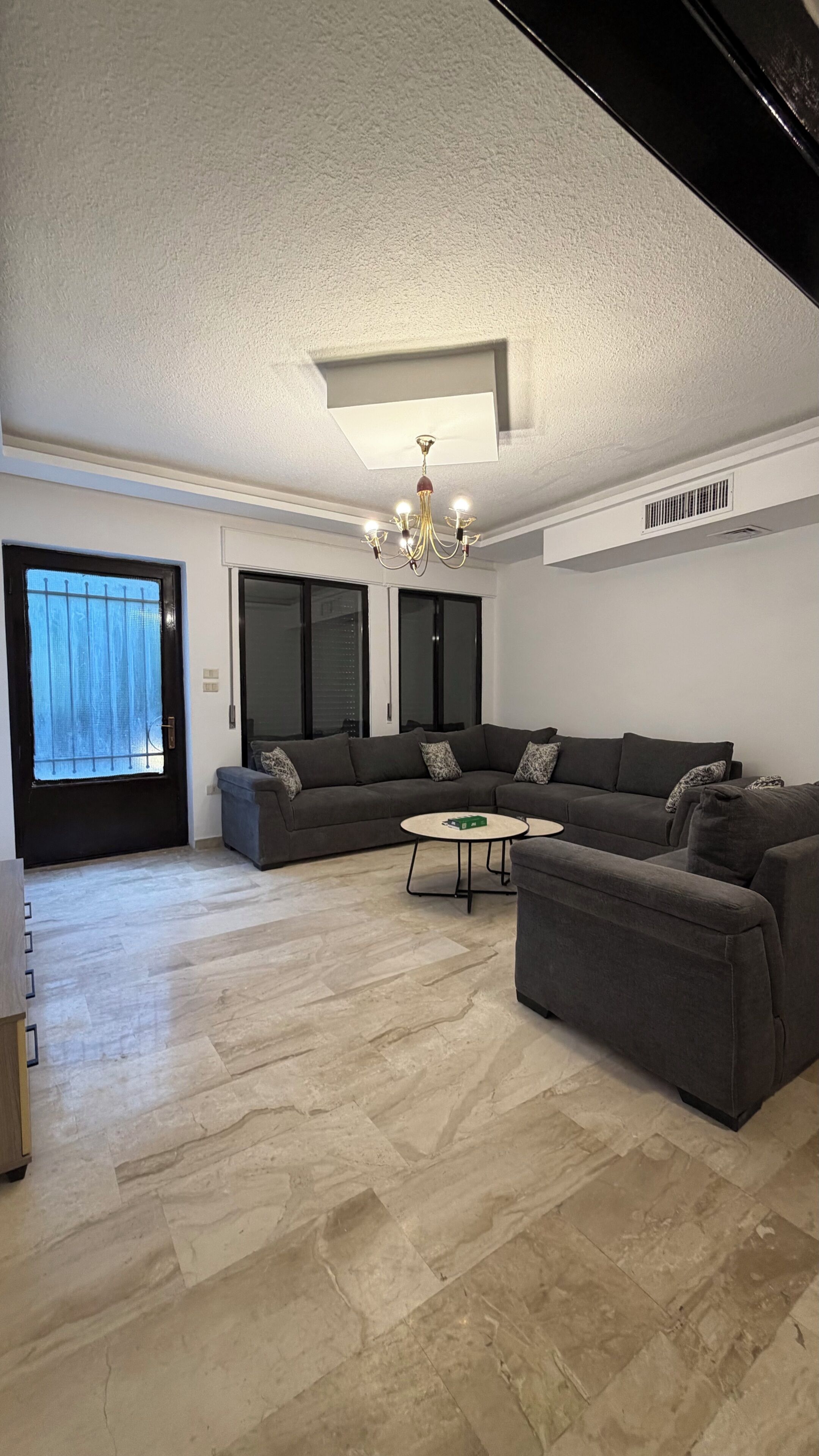 A spacious living room with a large sectional sofa, a round coffee table, and a chandelier.