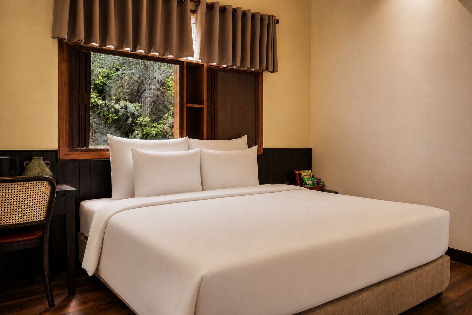 A neatly made bed with white linens, a wooden headboard, a wicker chair, a small table with a teapot, and a window with curtains.