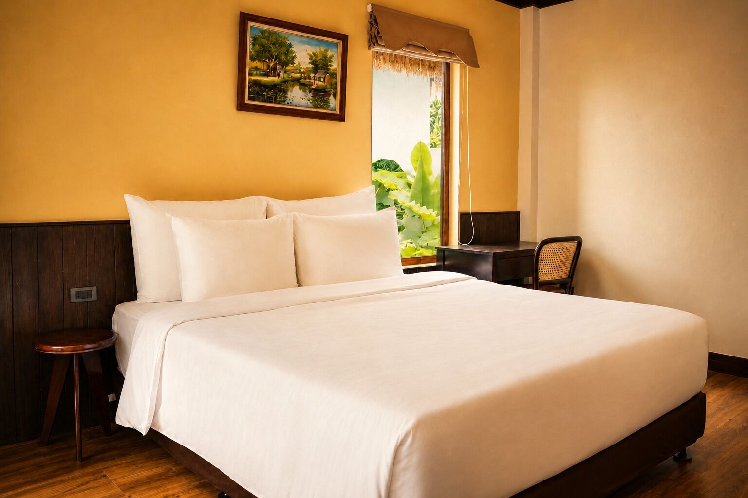 A neatly made bed with white linens, a small wooden stool, a desk with a chair, and a framed painting on the wall.