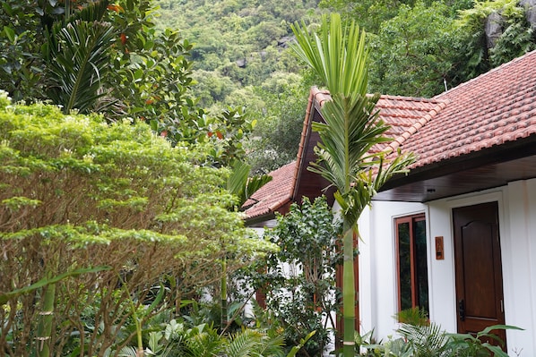 A house with a red-tiled roof, surrounded by lush greenery and a mountainous backdrop. - Moc An Village Tam Coc (Hoa Lu)