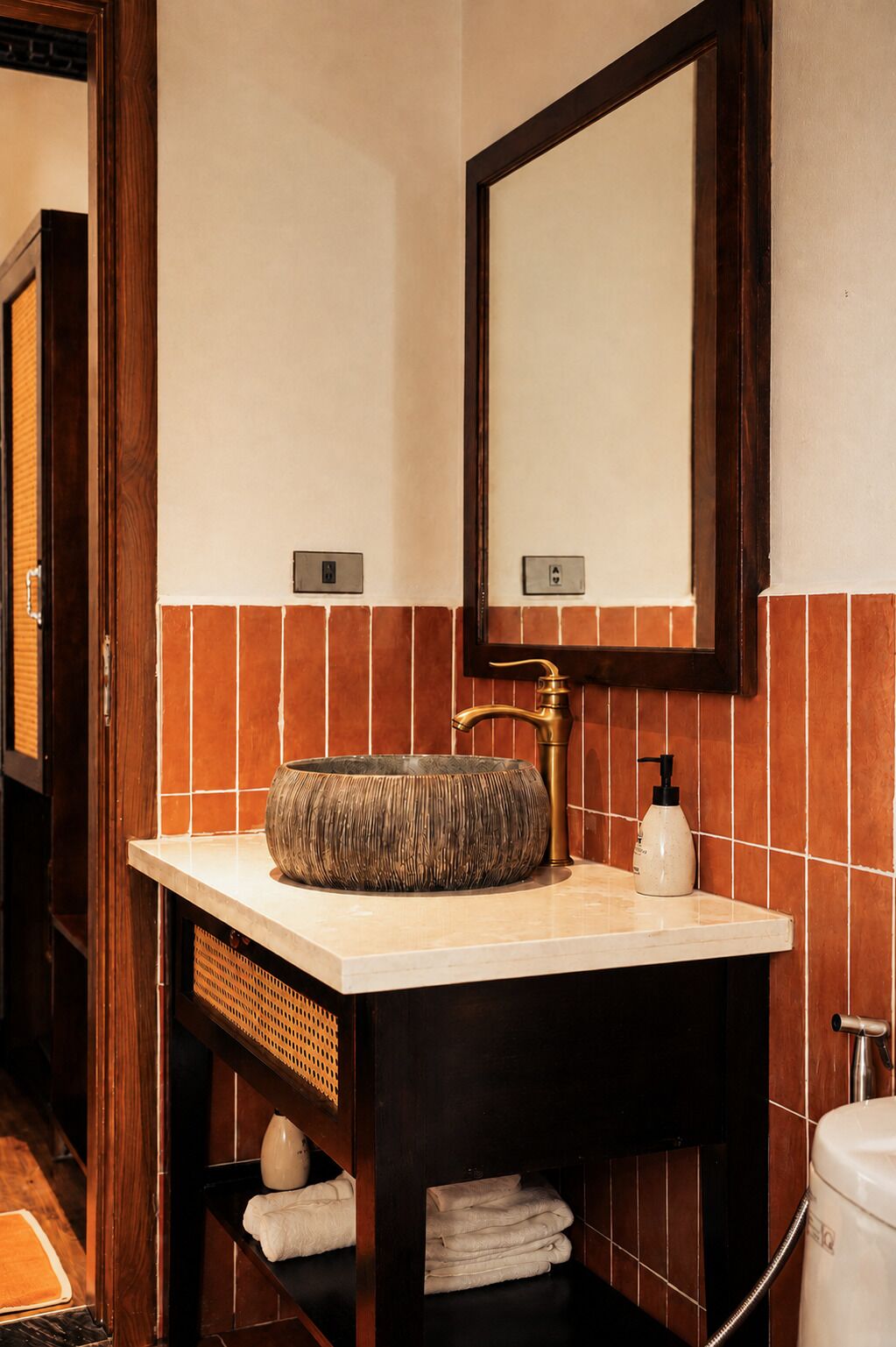 Een badkamer met een rond, geweven wastafel, een spiegel en een handdoekhouder.