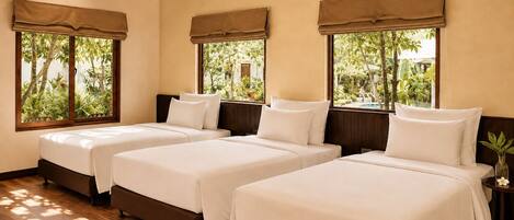 A hotel room with three beds, wooden flooring, and large windows with curtains.
