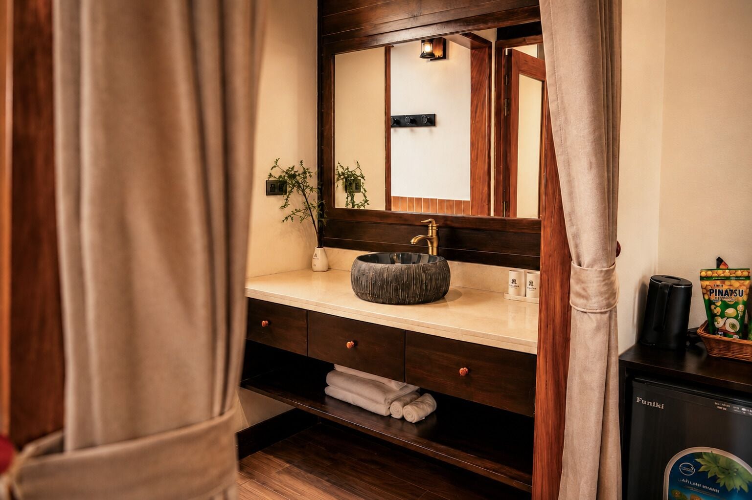 Un baño con tocador de madera, un lavabo redondo, un espejo, un perchero para toallas y una máquina de café.