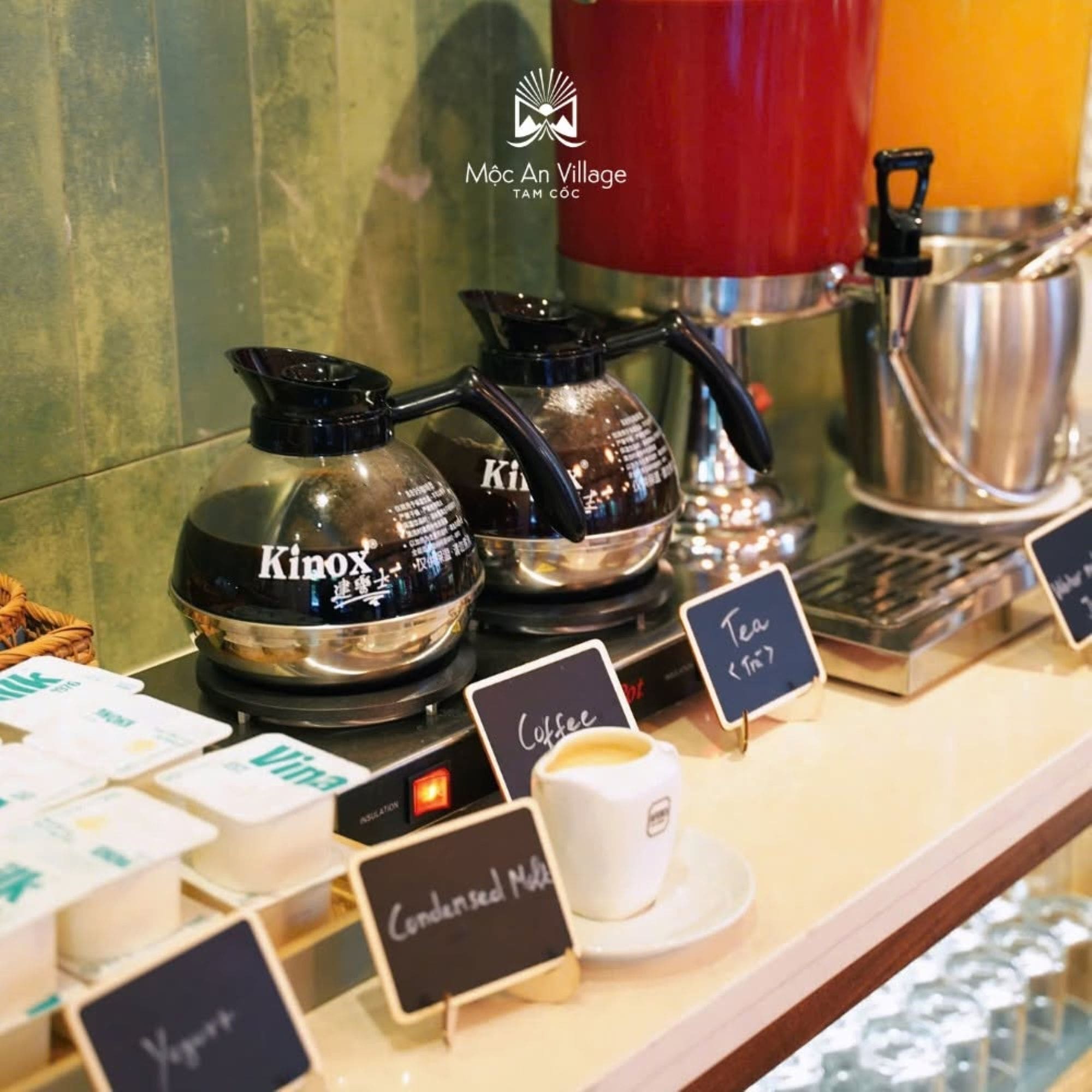 A coffee station with two KINOX coffee makers, a red kettle, and a cup of coffee labeled 'Condensed Milk.'