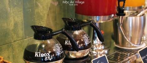 A coffee station with two KINOX coffee makers, a red kettle, and a cup of coffee labeled 'Condensed Milk.'