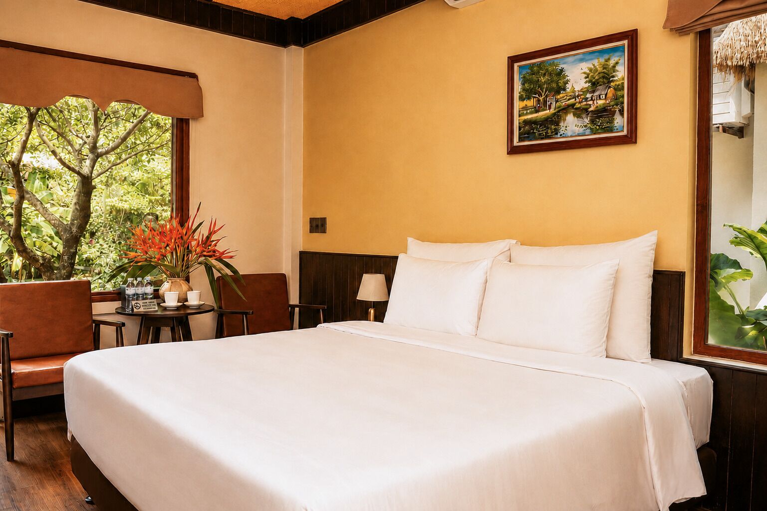 Une chambre d’hôtel avec un grand lit, une table à manger, des chaises, un tableau et une vue sur la verdure.