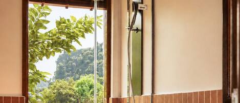 A bathroom with a toilet, shower, and a window with a view of greenery.