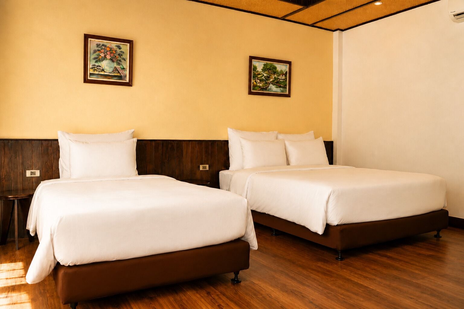 Een hotelkamer met twee bedden, houten vloeren en twee aan de muur hangende schilderijen.