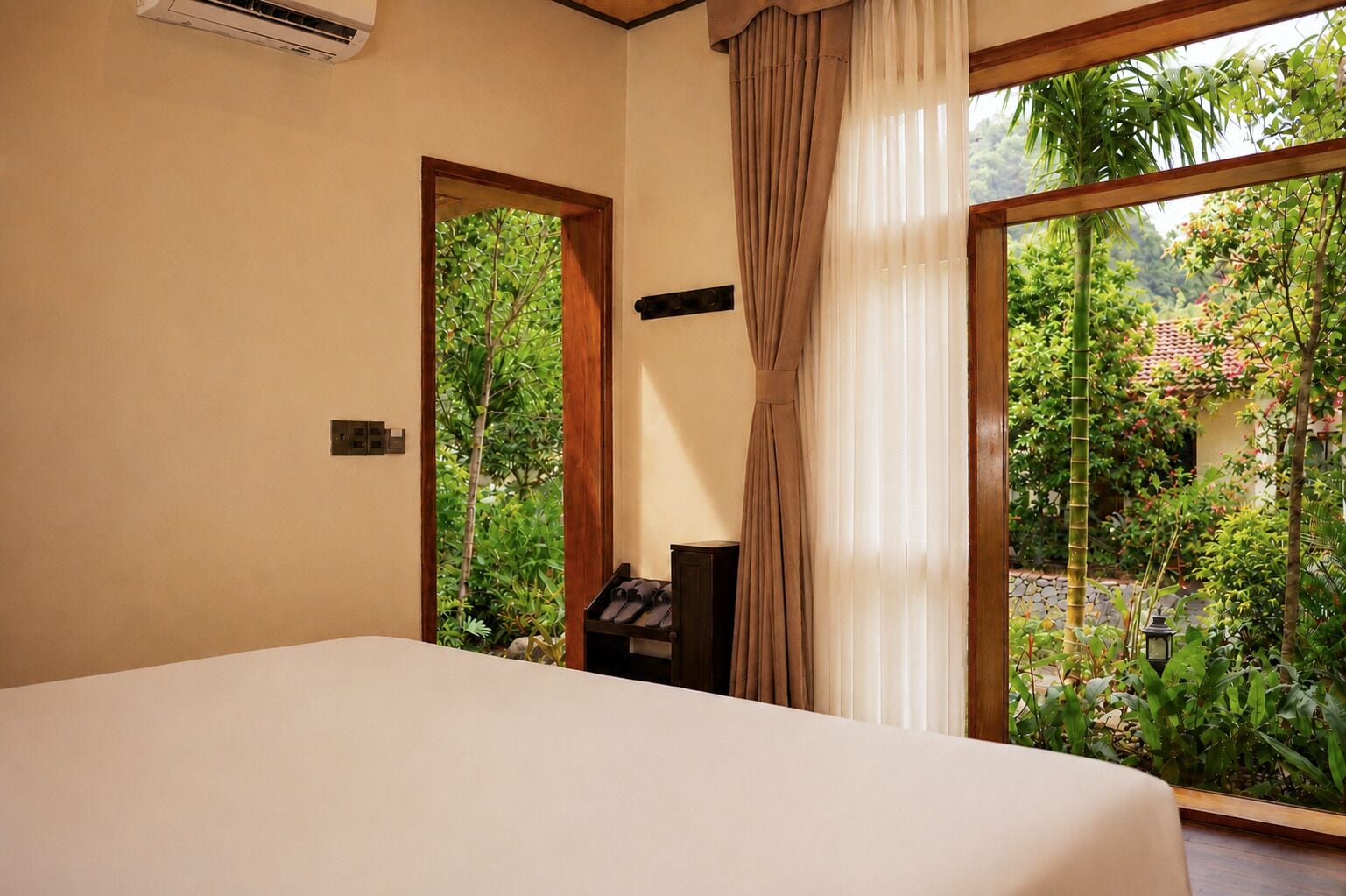 A bedroom with a bed, a nightstand, a window with curtains, and a view of greenery outside.