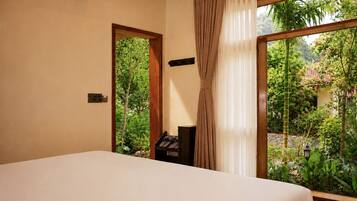 A bedroom with a bed, a nightstand, a window with curtains, and a view of greenery outside.