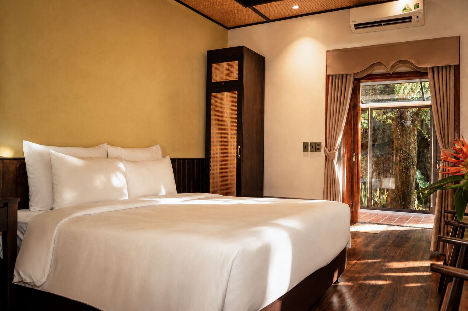 A large bed with white linens, a wooden headboard, and a window with curtains.