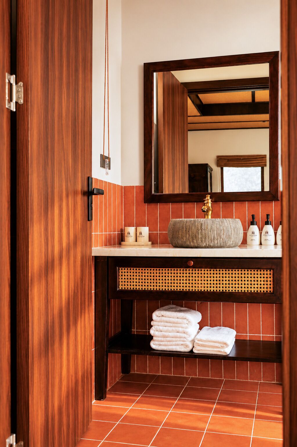 Un baño con puerta de madera, un espejo, un lavabo con grifo dorado y un perchero para toallas.