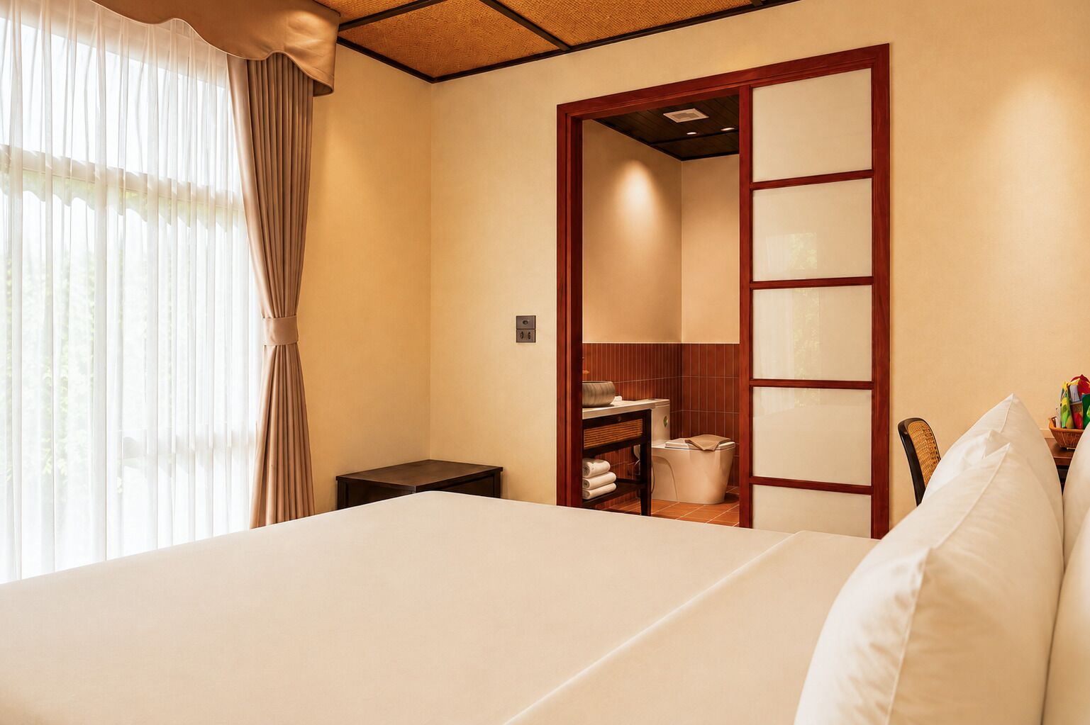 A hotel room with a bed, a wooden wardrobe, a small table, and a bathroom visible through a sliding door.