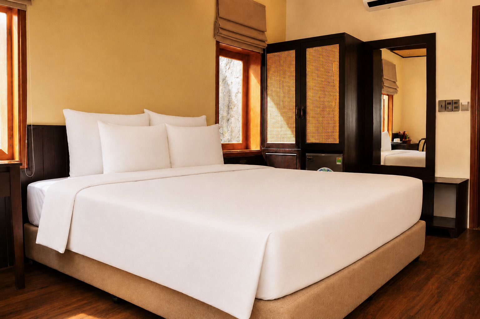 A large bed with white linens, a wooden headboard, and a nightstand with a lamp.