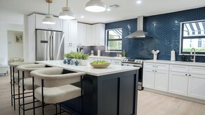 Una cocina moderna con una isla central, taburetes de bar, electrodomésticos de acero inoxidable y un salpicadero de azulejos azules.