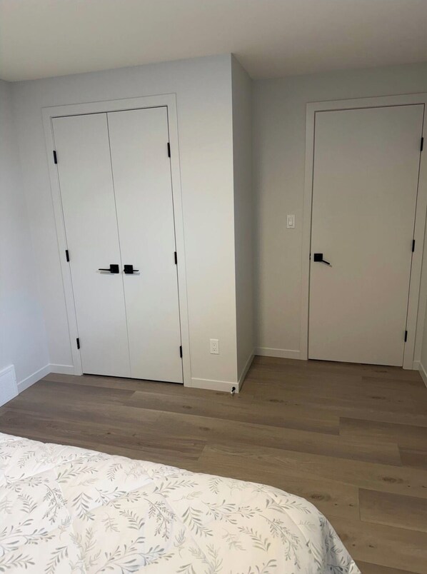 Een slaapkamer met een bed, twee witte inbouwkasten en een houten vloer.