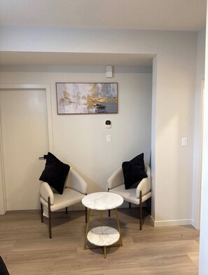 Une pièce comprenant deux fauteuils, une petite table ronde, un tableau accroché au mur et une porte.