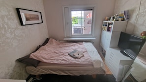 Une chambre à coucher avec un lit, une fenêtre, un radiateur, une télévision et une commode.