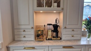 A kitchen with white cabinetry, a coffee maker, and a glass cabinet above the counter.