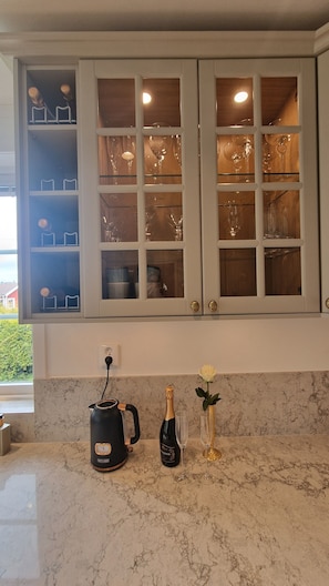 A kitchen with marble countertops, a coffee maker, a bottle of champagne, and a vase with a flower.