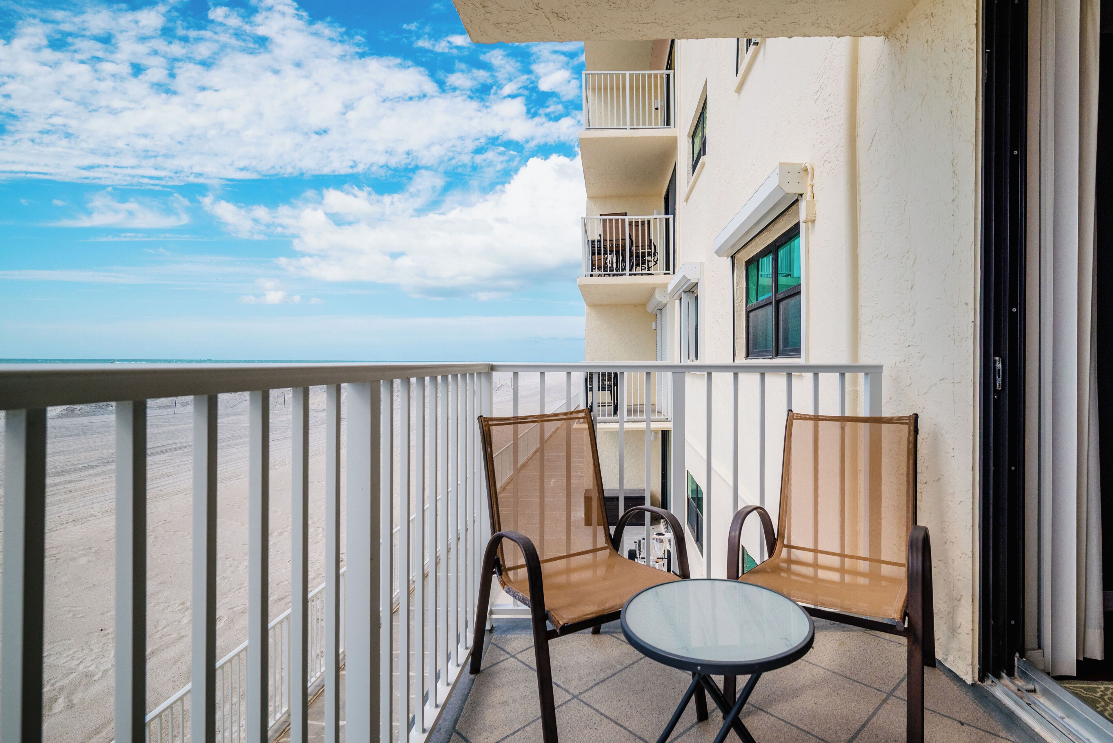A balcony with two chairs and a table, overlooking a beach.