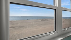 Une vue sur une plage, avec du sable et de l’eau, depuis une fenêtre.