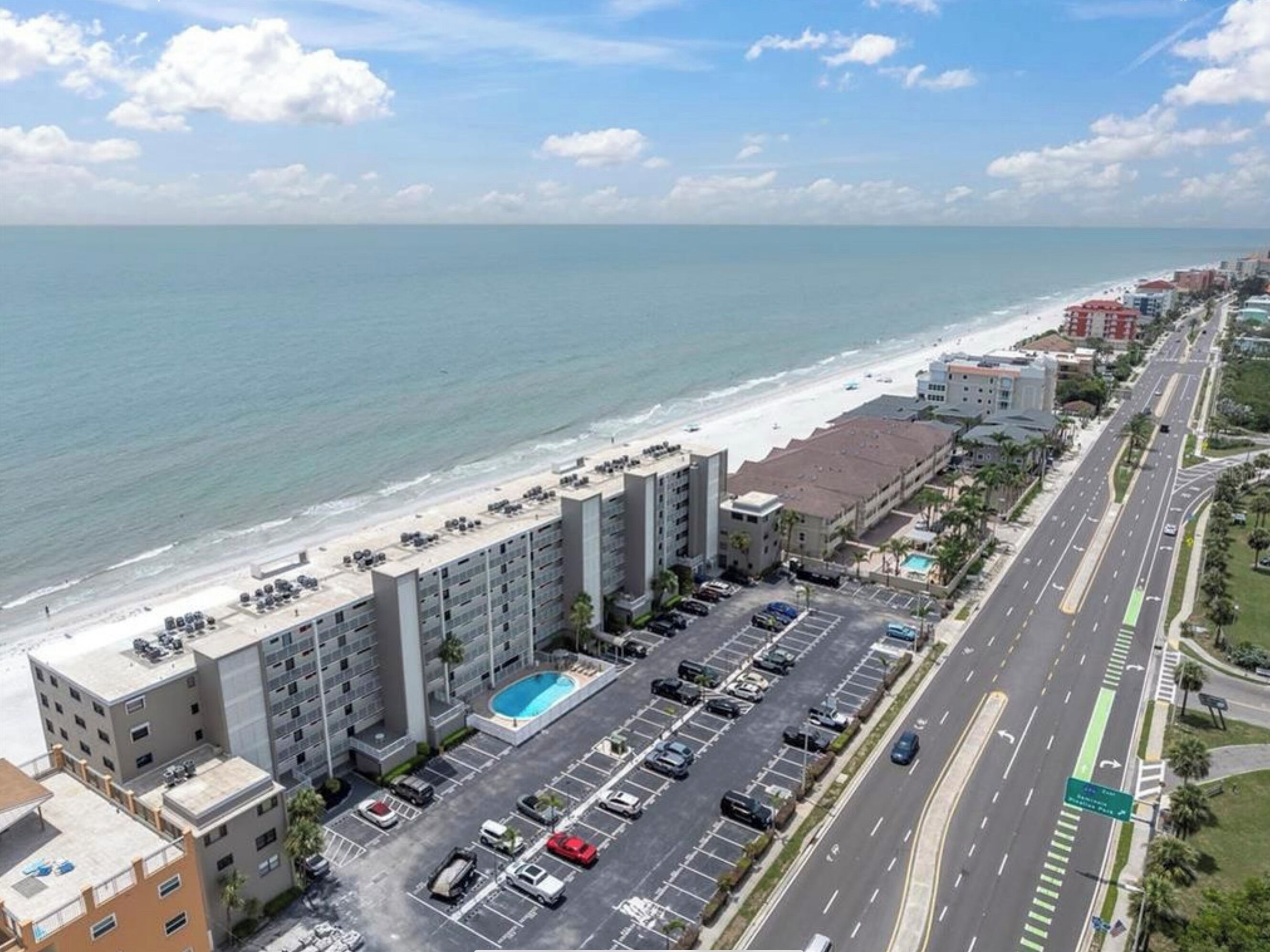 Ein Hotel an der Küste mit Parkplatz, Schwimmbad und Blick auf Strand und Meer.