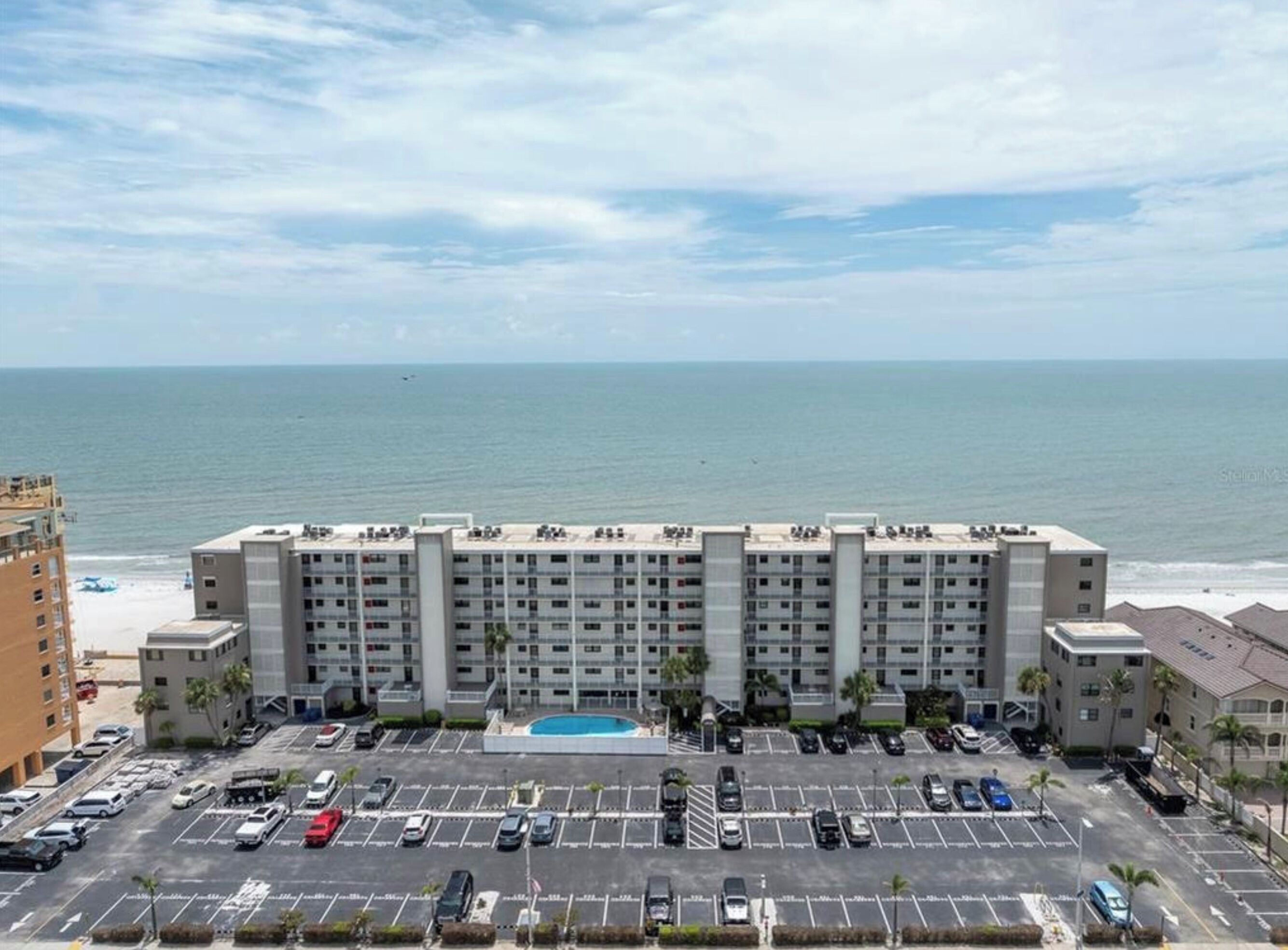 A hotel with multiple floors, a parking lot, and a view of the ocean.