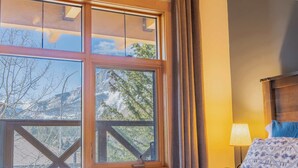 Ein Zimmer mit einem großen Fenster, einem Bett mit einem gemusterten Kissen, einer Lampe und einem hölzernen Kopfteil.