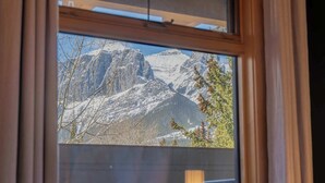 Ein Fenster mit Blick auf schneebedeckte Berge und kahle Bäume.