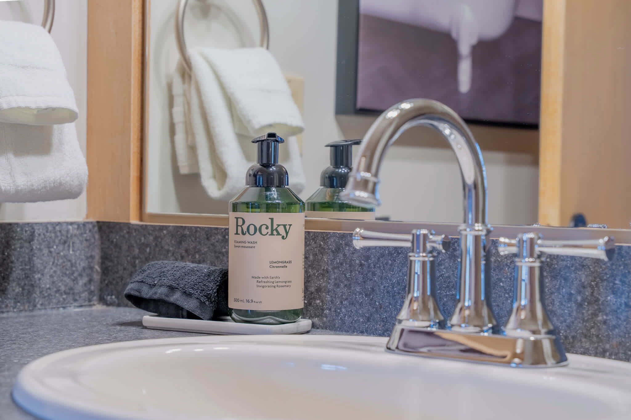 A bathroom sink with a bottle of Rocky soap, a towel, and a faucet.