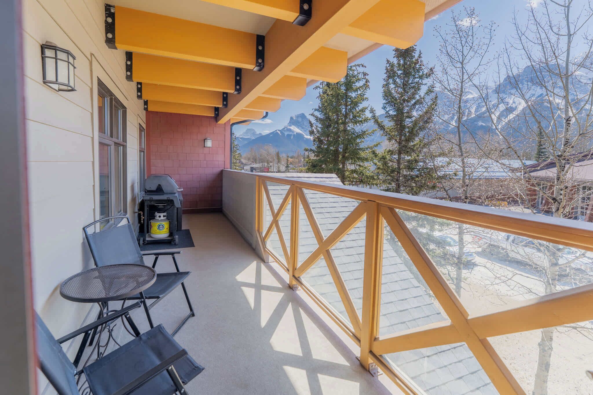 Un balcon avec un barbecue, des chaises et une vue sur des montagnes enneigées.