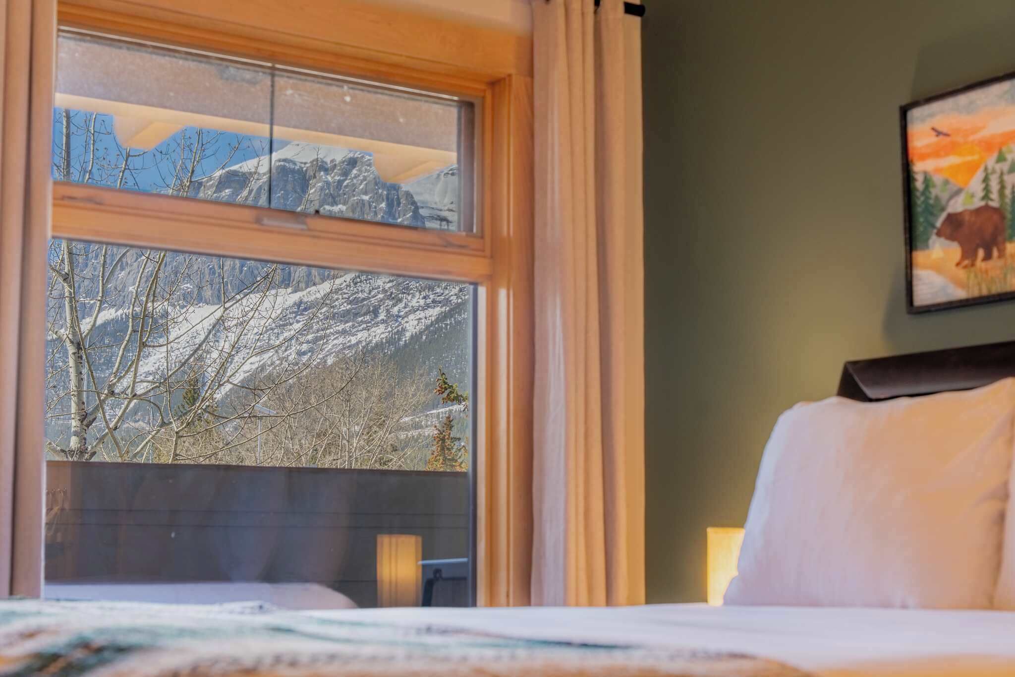 Een hotelkamer met een groot raam dat uitzicht biedt op de bergen, een bed en een schilderij aan de muur.