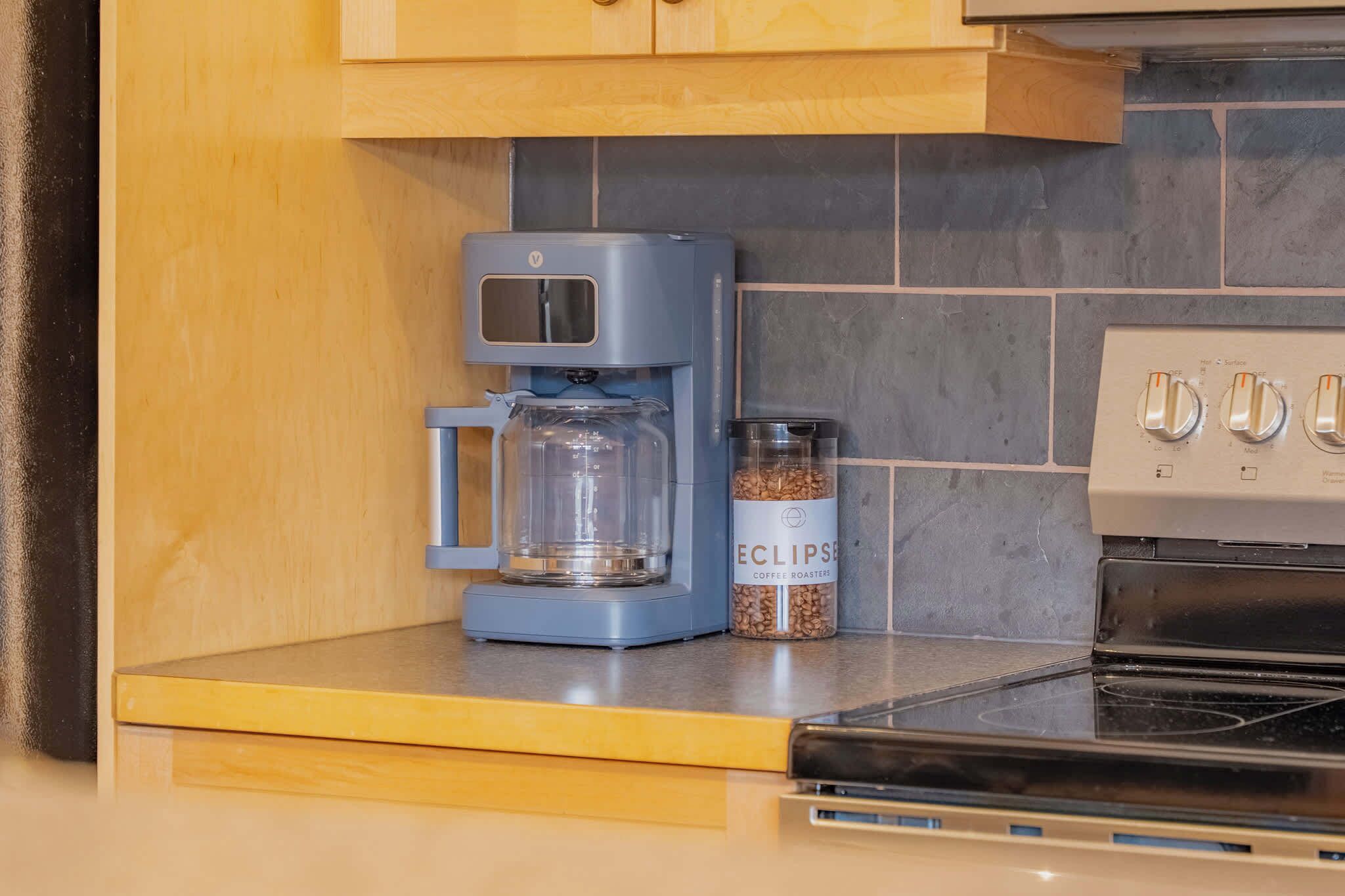 Une cuisine équipée d’une machine à café, d’une carafe en verre et d’un bocal de grains de café.