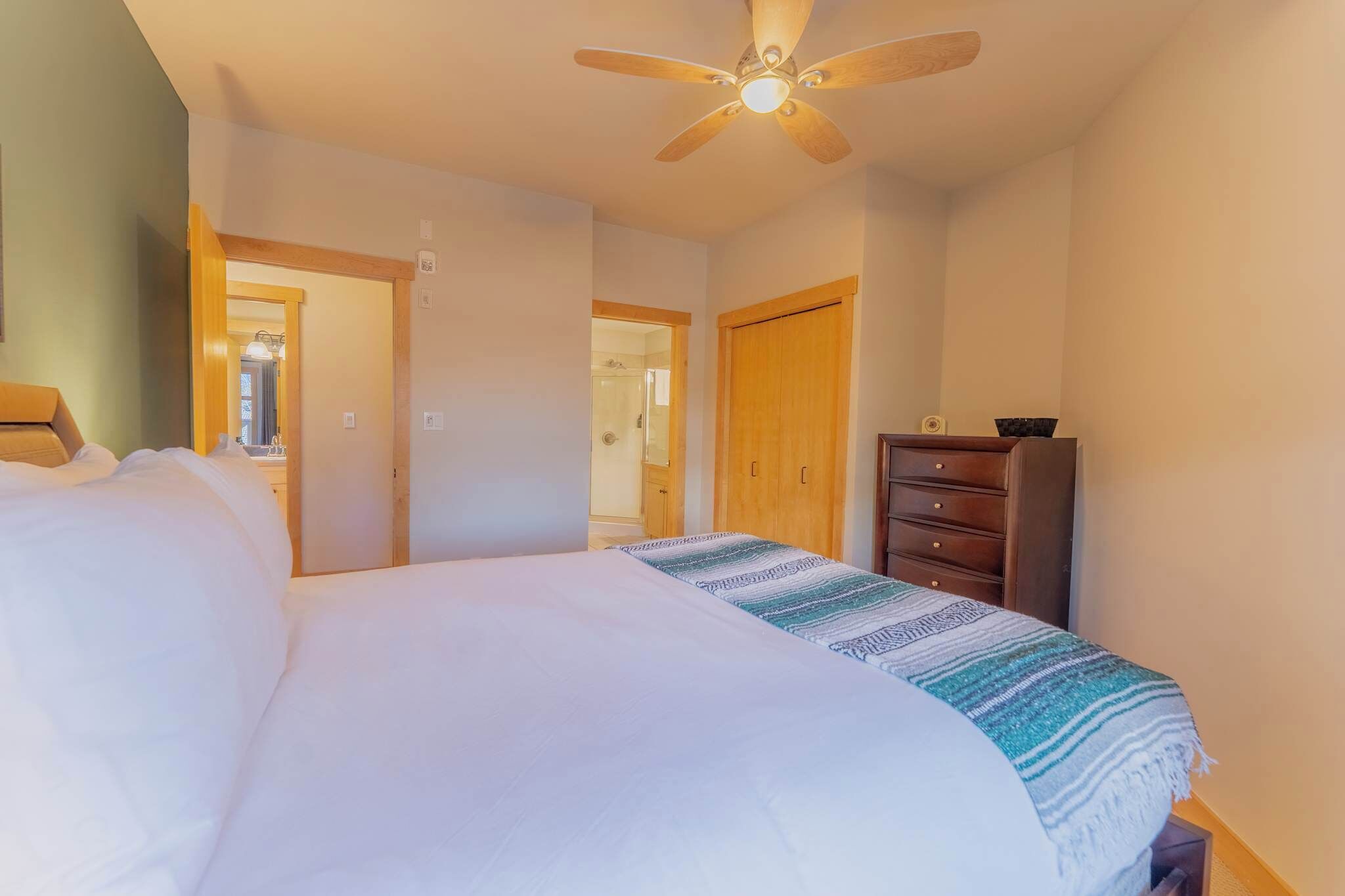 Ein Schlafzimmer mit Bett, Kommode, Deckenventilator und einer Tür zu einem anderen Raum.