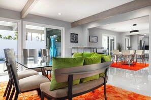 A modern living room with a glass dining table, a sofa with green cushions, and a bright orange rug. - Palm Springs 4BR | King Beds, Private Pool (Palm Springs)