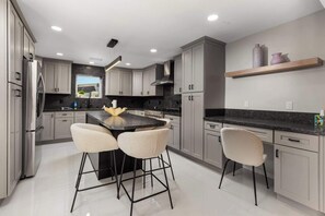 A modern kitchen with grey cabinets, a black island, and two bar stools. - Palm Springs 4BR | King Beds, Private Pool (Palm Springs)