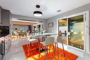 A modern kitchen with white cabinets, a black countertop, and a glass dining table with chairs. - Palm Springs 4BR | King Beds, Private Pool (Palm Springs)