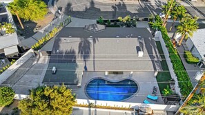 An aerial view of a building with a swimming pool, surrounded by trees and a curved road. - King beds, heated pool + cabana (Palm Springs)