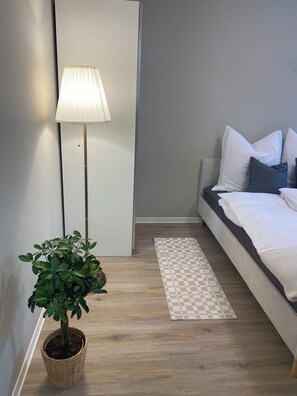 Ein Schlafzimmer mit einem Bett, Kissen, einer Stehlampe, einem Schachbrettteppich und einer Topfpflanze.