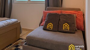 Une pièce comprenant un lit, un canapé, une fenêtre avec des rideaux et un tapis à motifs.