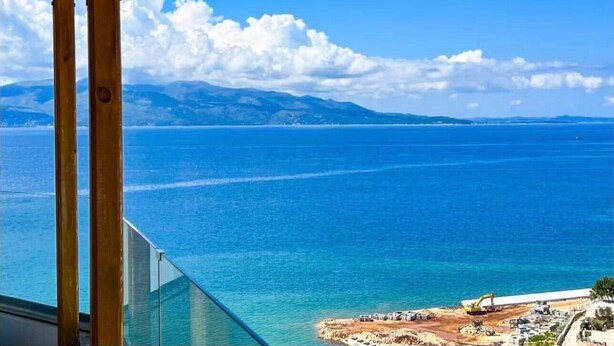 Une vue sur la mer depuis un balcon orné de piliers en bois, avec un ciel dégagé et des montagnes à l’horizon.