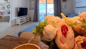 Un salon moderne doté d’un téléviseur à écran plat, d’une table à manger agrémentée d’un vase de fleurs et d’un balcon offrant une vue agréable.