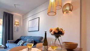 Un coin repas avec une table en bois, des sets de table en fibres tressées, une bouteille de vin, des verres et un vase de fleurs.