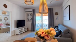 Un salon moderne avec un téléviseur, un canapé et une table basse en bois sur laquelle est posé un vase de fleurs.