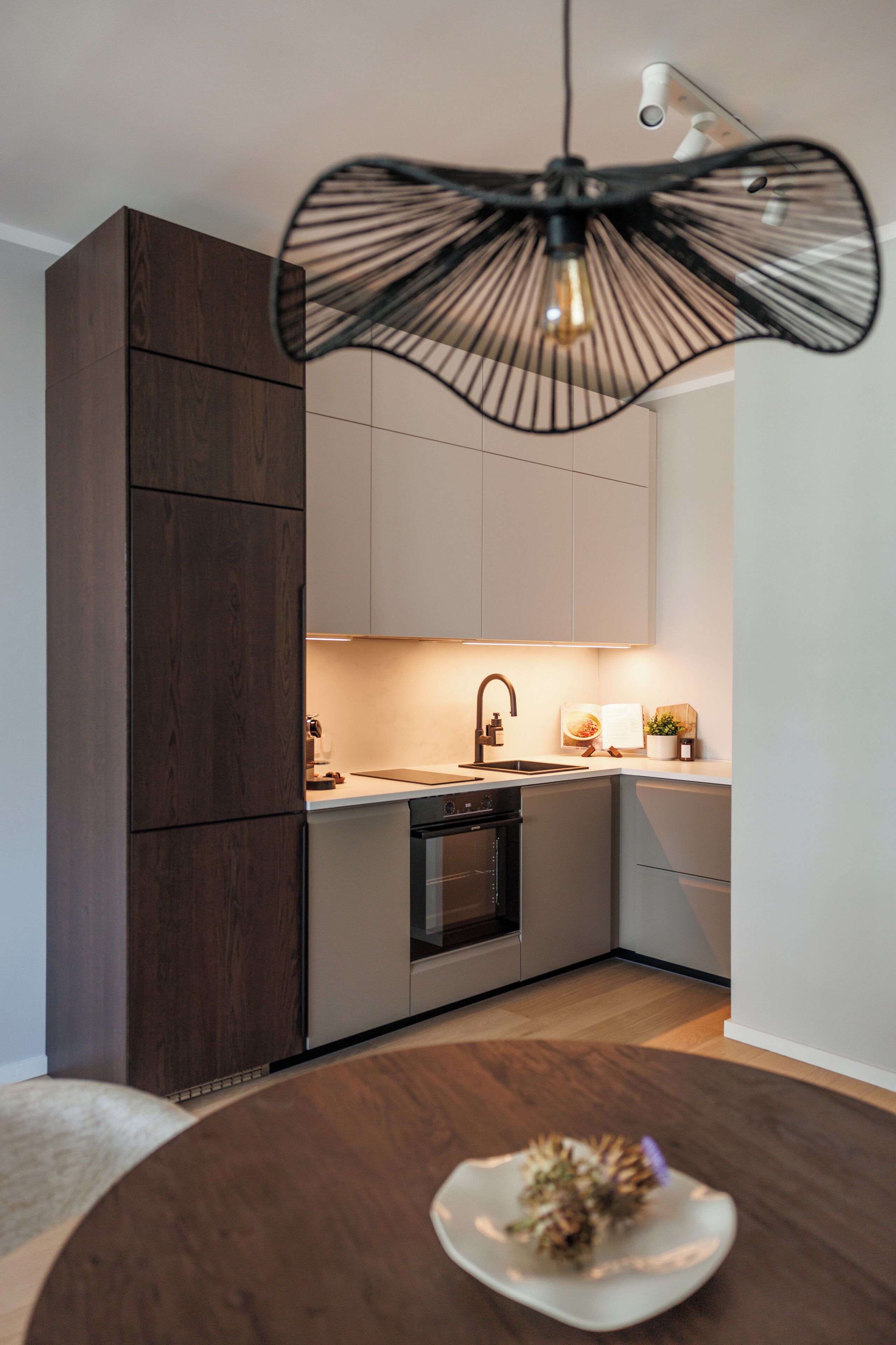 Una cocina moderna con armarios de madera oscura, una encimera blanca, una campana extractora negra y una mesa redonda con un objeto decorativo.