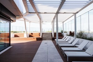 Eine Dachterrasse mit einer Pergola, Liegestühlen und Blick auf die Stadt.