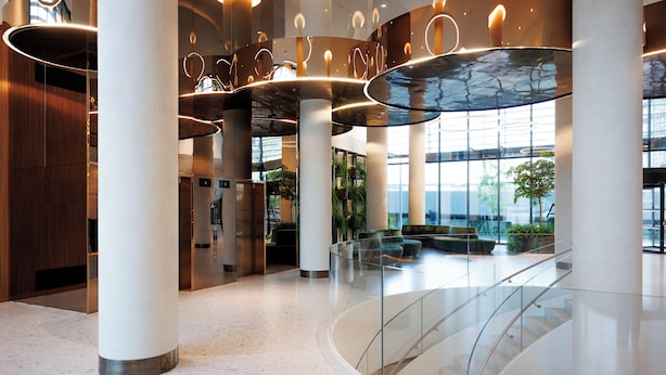 A modern lobby with a curved glass railing, large columns, and a central staircase. - Skyline Suite - Danube-View Balcony&Pool (Vienna)