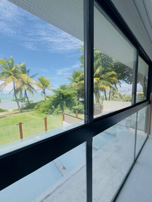 A modern building with large windows overlooking a beach with palm trees and a clear sky. - Beachfront Retreat: Premium Escape with Direct Beach Access (João Pessoa)